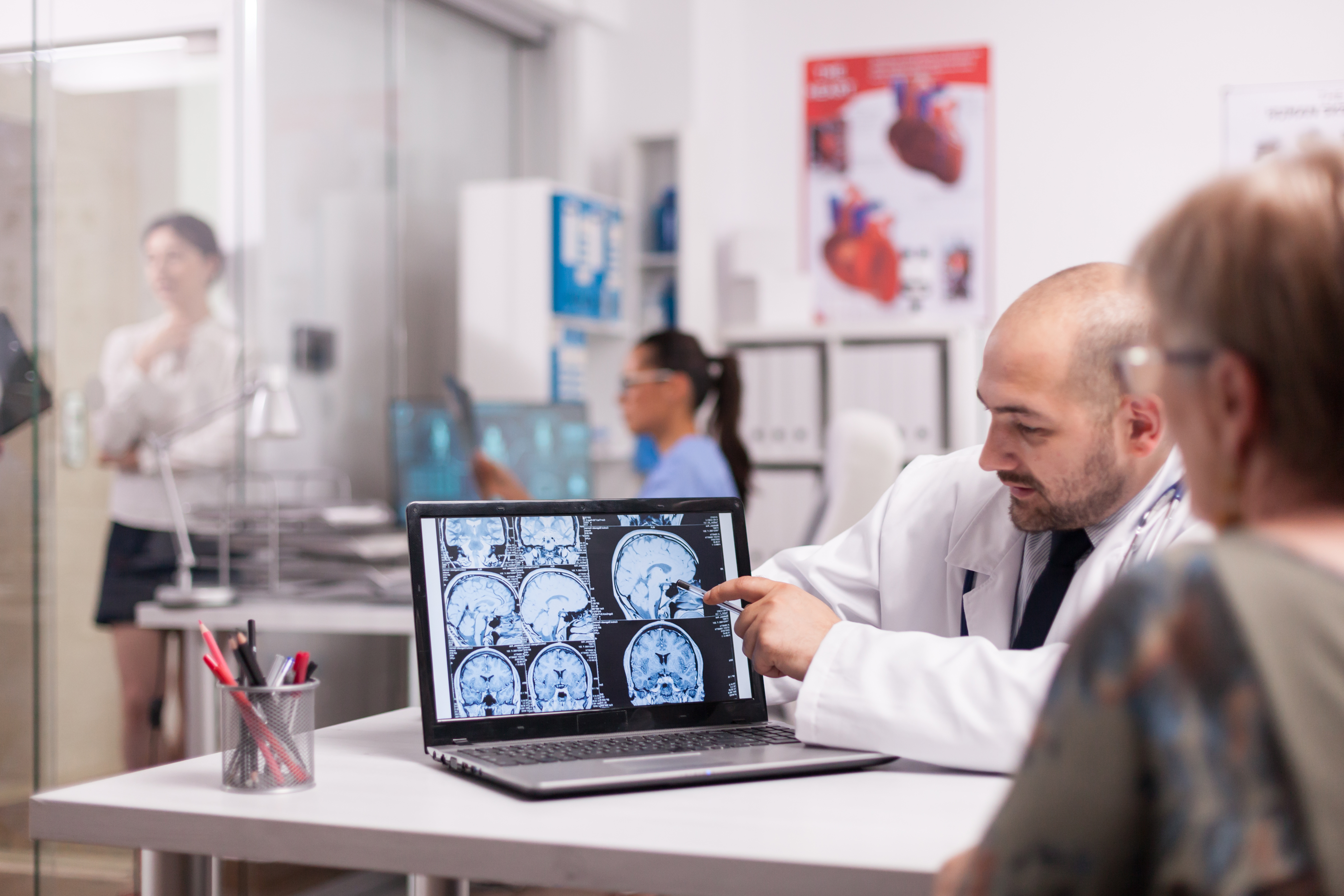 Man in white coat in conversation with a female patient while pointing at a laptop screen with a brain scan image