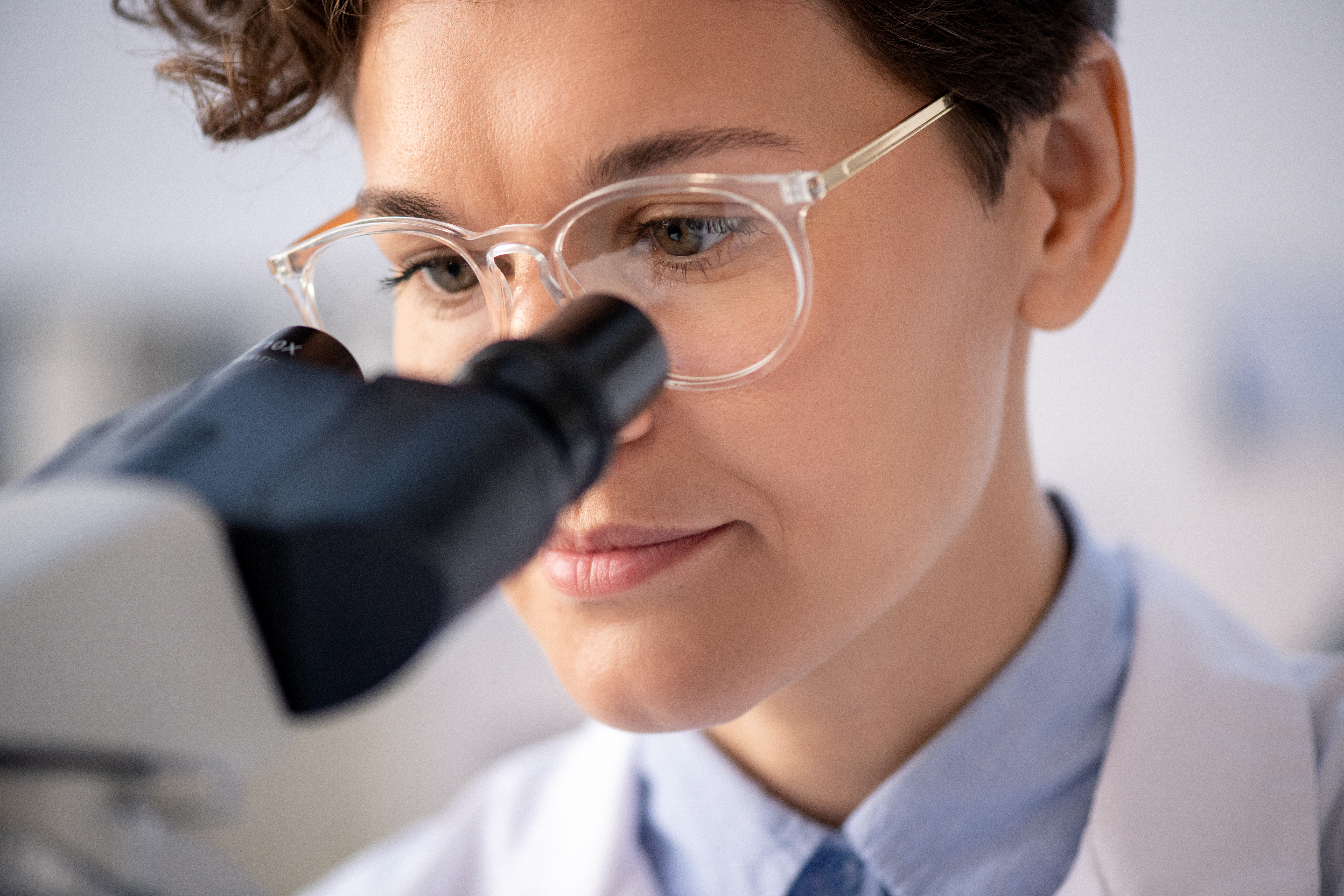 A scientist in eyeglasses and whitecoat looking through a microscopy eyepiece (source:envato)